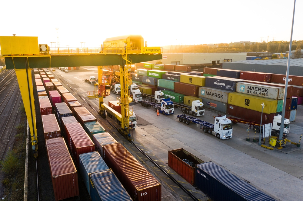 Railyard with stacked containers and intermodal trucks in the loading area