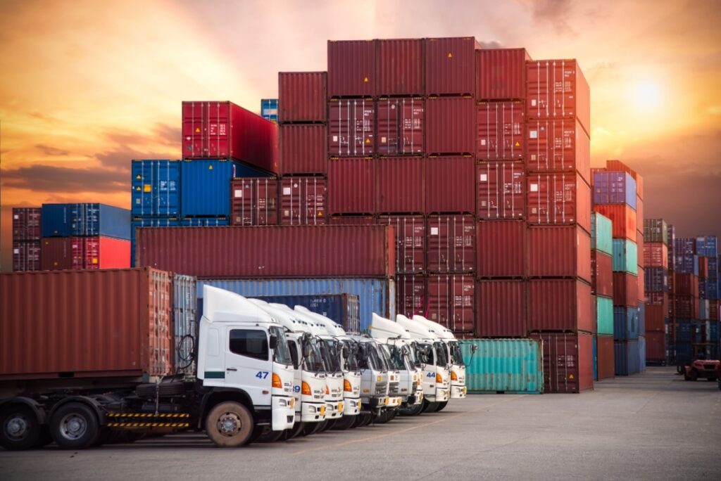 Drayage trucks parked at the port yard next to stacked containers